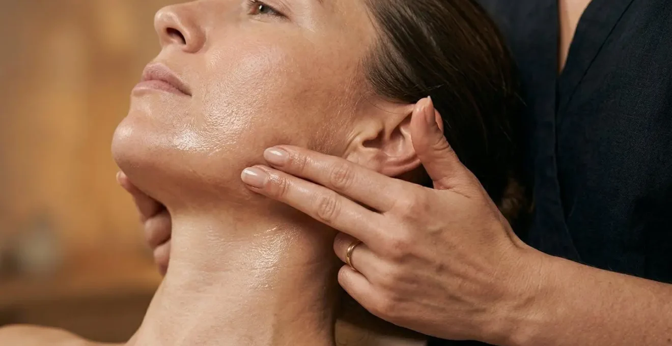 Mains appliquant une huile de massage sur la zone de la mâchoire avec technique circulaire